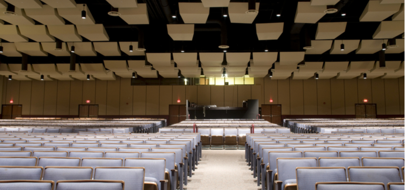 A conference room with accoustic baffles ceiling, stage and audience chairs.